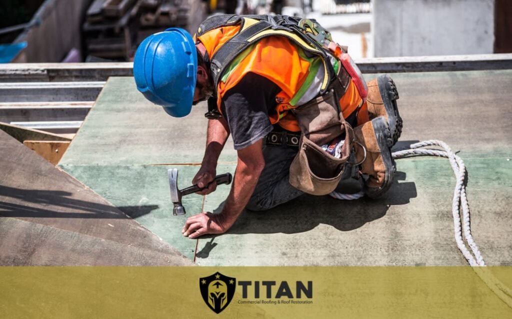 A construction worker in a blue helmet and safety vest uses a hammer on a rooftop. The Titan Commercial Roofing & Roof Foundation logo is at the bottom of the image.