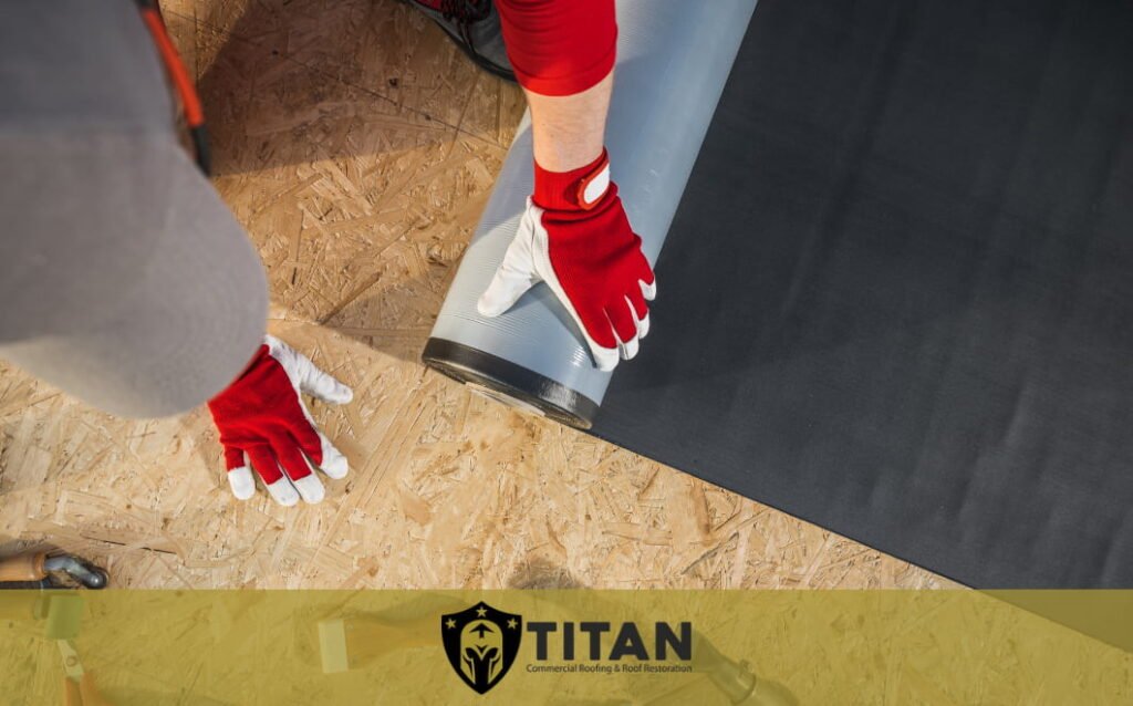 Person wearing red gloves unrolling roofing material onto a wooden surface; Titan Commercial Roofing & Roof Restoration logo is visible at the bottom.